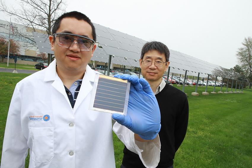 阎发，博士.D.宋兆宁博士.D.他站在一片太阳能电池板上. Dr. 宋兆宁拿着一块太阳能电池对着镜头.